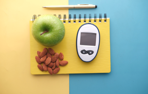 a glucose monitor and a healthy snack sitting atop a closed notebook
